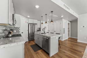Kitchen with tasteful backsplash, dark wood-style floors, stainless steel appliances, light stone counters, and a kitchen island with sink