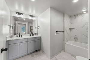 Bathroom with light marble finish floors, double vanity, and shower / washtub combination