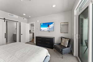 Carpeted bedroom featuring a barn door, ensuite bathroom, and recessed lighting