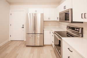 Kitchen with appliances with stainless steel finishes, light countertops, white cabinetry, and light wood-type flooring