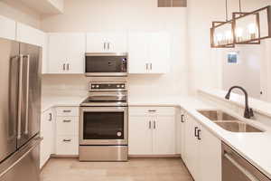 Kitchen featuring appliances with stainless steel finishes, decorative light fixtures, white cabinetry, light wood-type flooring, and light stone counters