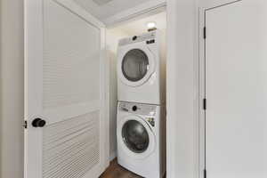 Washroom featuring stacked washing machine and dryer and dark wood-style flooring