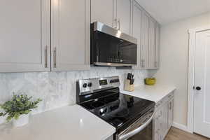 Kitchen with gray cabinetry, stainless steel appliances, decorative backsplash, a textured ceiling, and light wood-style flooring