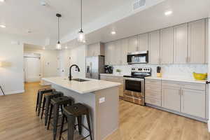 Kitchen with appliances with stainless steel finishes, gray cabinets, a center island with sink, light wood-type flooring, and recessed lighting