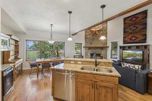 Kitchen featuring light stone counters, brown cabinets, a stone fireplace, hanging light fixtures, and light wood-style floors