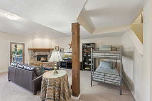 Living area featuring a stone fireplace, carpet flooring, and a textured ceiling
