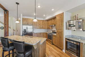 Kitchen featuring beverage cooler, appliances with stainless steel finishes, tasteful backsplash, light wood-style flooring, and pendant lighting