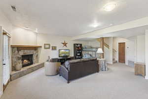 Carpeted living area with a stone fireplace, stairs, and a textured ceiling