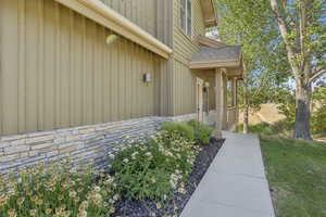 View of exterior entry with stone siding, a shingled roof, a lawn, and board and batten siding