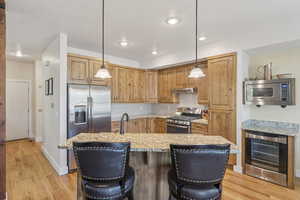 Kitchen featuring decorative backsplash, stainless steel appliances, light wood-style floors, beverage cooler, and pendant lighting
