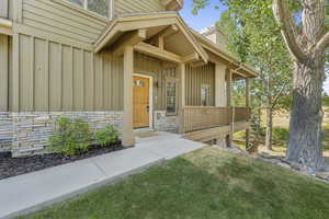 Entrance to property featuring board and batten siding, stone siding, covered porch, and a yard