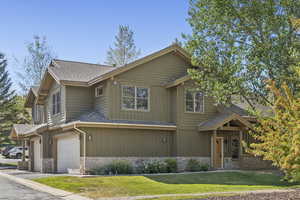 View of front facade featuring stone siding, a shingled roof, a garage, a front yard, and asphalt driveway