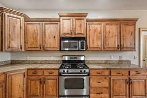 Kitchen featuring appliances with stainless steel finishes, light stone countertops, and brown cabinets