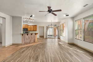 Unfurnished living room featuring healthy amount of natural light, a chandelier, ceiling fan, wood finish floors, and a textured ceiling