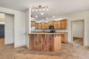 Kitchen with a kitchen bar, a peninsula, brown cabinets, light stone counters, and stainless steel appliances