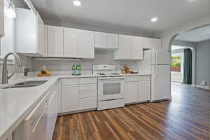 Kitchen featuring white cabinets, white appliances, dark wood-style floors, arched walkways, and light stone countertops