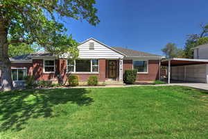 View of front facade featuring a front lawn, brick siding, a shingled roof, and an attached carport