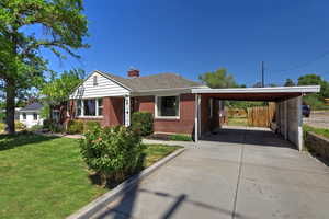 Bungalow-style home featuring a carport, brick siding, driveway, a chimney, and a shingled roof