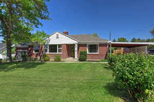 View of front of property featuring a chimney, brick siding, a front lawn, roof with shingles, and a carport