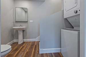 Laundry room featuring stacked washing machine and dryer and dark wood-style flooring
