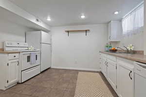 Kitchen with white cabinets, white appliances, light countertops, open shelves, and recessed lighting
