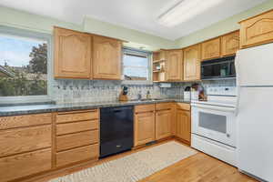 Kitchen featuring black appliances, open shelves, light wood-style flooring, dark countertops, and decorative backsplash
