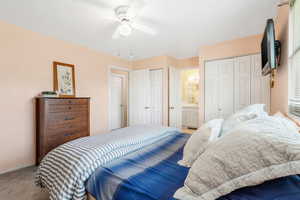 Carpeted bedroom featuring multiple closets, ceiling fan, and connected bathroom