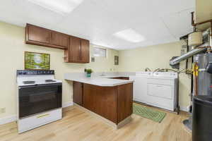 Kitchen featuring white range with electric cooktop, a drop ceiling, light countertops, a peninsula, and light wood-style floors also the laundry