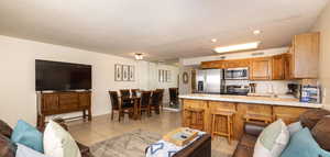 Kitchen with open floor plan, tile countertops, brown cabinetry, light tile patterned flooring, and appliances with stainless steel finishes