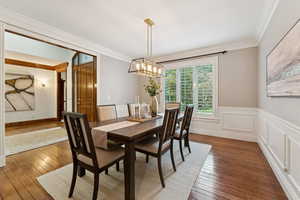 Dining area featuring ornamental molding, hardwood / wood-style floors, wainscoting, and a chandelier