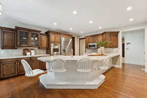 Kitchen with glass insert cabinets, tasteful backsplash, a kitchen bar, stainless steel appliances, and recessed lighting