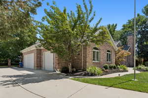 View of front of home featuring concrete driveway, brick siding, a chimney, and an attached garage