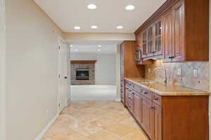 Kitchen featuring glass insert cabinets, brown cabinets, tasteful backsplash, light stone counters, and a fireplace