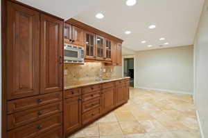 Kitchen with decorative backsplash, recessed lighting, brown cabinets, glass insert cabinets, and light stone counters