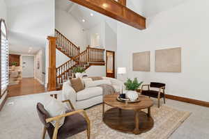 Living area featuring high vaulted ceiling, beam ceiling, light colored carpet, stairs, and recessed lighting