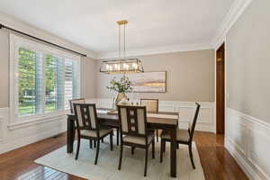 Dining space with dark wood-style flooring, ornamental molding, a wainscoted wall, and a decorative wall