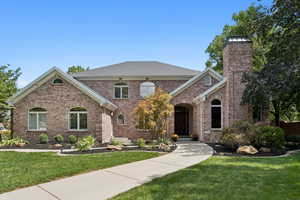 View of front facade featuring brick siding, a front lawn, and a chimney