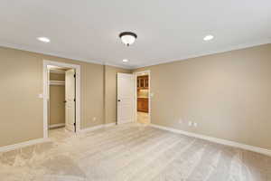 Unfurnished bedroom featuring recessed lighting, light carpet, a walk in closet, and crown molding