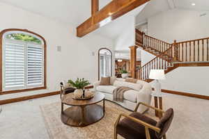 Living area with carpet, beamed ceiling, high vaulted ceiling, stairs, and decorative columns