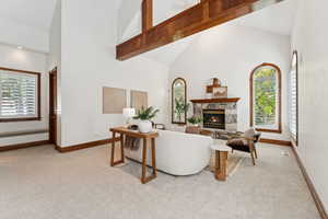 Living area with light carpet, high vaulted ceiling, a stone fireplace, and healthy amount of natural light
