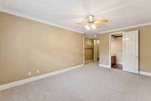 Unfurnished bedroom with crown molding, carpet, a spacious closet, ceiling fan, and ensuite bath