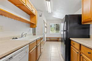 Kitchen featuring dishwasher, light countertops, a textured ceiling, freestanding refrigerator, and open shelves
