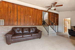 Living room with a ceiling fan, light colored carpet, a textured ceiling, light tile patterned floors, and stairs