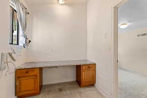 Unfurnished office with built in desk, a textured ceiling, and light colored carpet