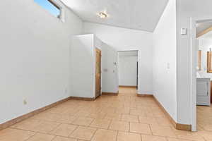 Bonus room with vaulted ceiling, a textured ceiling, light tile patterned floors, and washer / clothes dryer