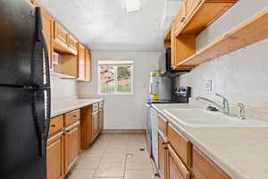 Kitchen featuring black appliances, light tile patterned floors, light countertops, brown cabinets, and a textured ceiling