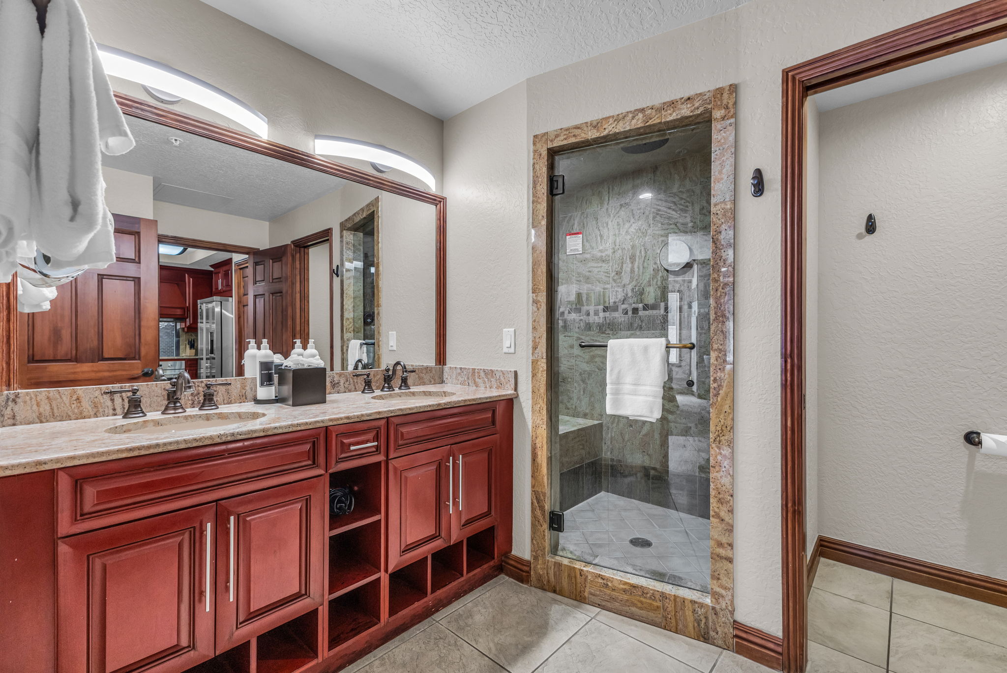 Full bath featuring a textured ceiling, light tile patterned floors, a shower stall, double vanity, and a textured wall
