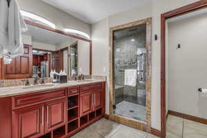 Full bath featuring a textured ceiling, light tile patterned floors, a shower stall, double vanity, and a textured wall