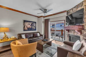 Living area with wood finished floors, crown molding, ceiling fan, and a stone fireplace