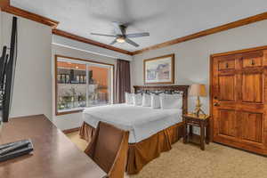 Bedroom with a textured ceiling, a textured wall, light colored carpet, crown molding, and ceiling fan